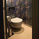 Touche d’exotisme dans les toilettes suspendues avec chasse d’eau intégrée et placard de rangement aux murs revêtus d’un papier peint inattendu très seventies (modèle Sunbird, création Matthew Williamson, chez Osborne & Little).