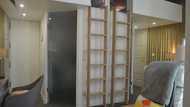 La porte en verre sablé cache la salle de bains installée sous la mezzanine. L’échelle, qui se reflète dans les portes miroitées, permet d’accéder à la chambre.