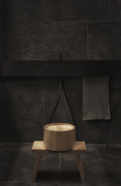 Seul le banc de bois traditionnel et le bassin rappellent de la fonctionnalité de la salle de bains qui garde tout son mystère derrière un mur de pierre rugueuse.