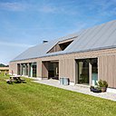 Les abords de la maison sont recouverts de pavés en pierre naturelle qui dessine un chemin pour la contourner et tranche avec l’herbe verte du plat pays...