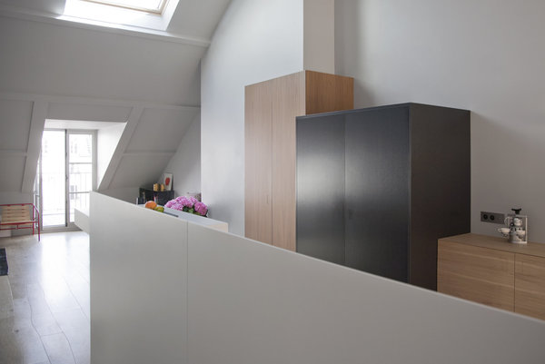 Rue d’Aboukir, l’espace cuisine est dissimulé derrière une crédence en bois laqué accueillant un plan de travail intégrant évier et plaque de cuisson. En arrière-plan, un jeu de boîtes de formats différents a été réalisé sur mesure : la première, à cheval sur le conduit de cheminée intègre un grand réfrigérateur et un vaisselier. La seconde boite en métal noirci permet, grâce à ses portes rabattables de libérer un second plan de travail et du rangement. Et la troisième repart en noyer et de façon linéaire.