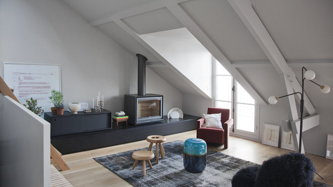 Le poêle à bois a été installé sur une banquette de marbre noir, sur laquelle repose un meuble de rangement réalisé sur mesure. Mobilier sélectionné chez Siltec, tabourets de berger dessinés par Charlotte Perriand (Cassina) sur un tapis d’inspiration orientale Reloaded (Golran).