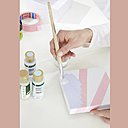 Etape 2 : à l’aide d’un pinceau, peignez l’intérieur de ces triangles de différentes couleurs, sans oublier les côtés du couvercle. Prenez soin de peindre à partir de l’intérieur du ruban Tesa® vers l’extérieur pour ne pas que la peinture puisse passer sous le ruban en cas de mauvaise pose. Laissez sécher.