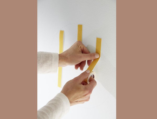 Etape 3 : sur le mur, à l’emplacement de la rosace auparavant délimité et nettoyé, collez des bandes verticales de ruban adhésif double face, Fixer Objet Spécial Intérieur de chez Tesa®.