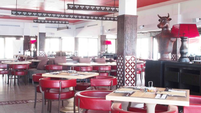 Le rouge est mis dans le restaurant qui offre une spécialité de viandes. Au sol, un grès cérame imitant une pierre et des bandes de carreaux ciment à motifs géométriques.