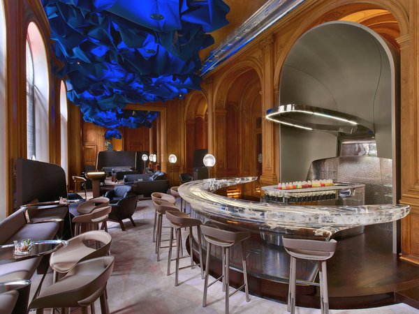 Stéphane Corler donne au Bar du Plaza Athénée une dimension onirique et mystérieuse, en installant ce drapé bleu profond qui invite à la rêverie et crée un ciel imaginaire. Le bar en résine coulée a été réalisé par D3 actuel JM Tech, société spécialisée dans la construction automobile.