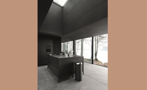 La cuisine est aménagée en îlot, les placards et les fours de cuisson sont à la verticale. Le noir mat est le parti pris choisi tout au long des pièces dans une belle et sobre unité chromatique.