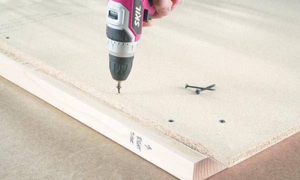 Etape 6 : fixez les panneaux derrière les deux structures latérales que vous avez réalisées à l’étape 4. Posez la structure sur le panneau de façon à l’aligner avec le bord inférieur et le bord arrière, en laissant dépasser une longueur de 3,81 cm du panneau de particules en haut et une longueur de 2 cm du tasseau de 38 mm x 89 mm sur le devant. Placez les vis aux quatre coins et au milieu de chaque côté de votre structure.