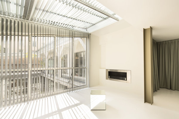 La verrière éclaire les murs et les plafonds de l’appartement rappelant l’origine du lieu. Sa lumière est adoucie par un store à lames métalliques qui dessinent une trame sur le sol.