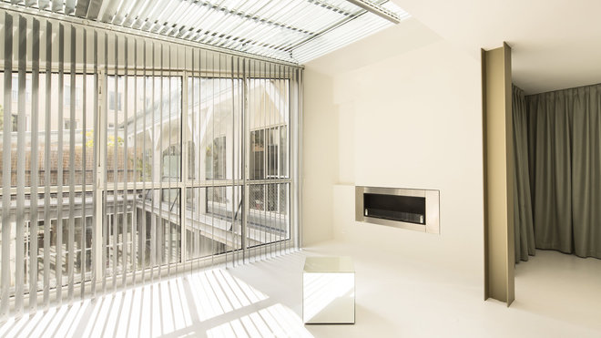 La verrière éclaire les murs et les plafonds de l’appartement rappelant l’origine du lieu. Sa lumière est adoucie par un store à lames métalliques qui dessinent une trame sur le sol.