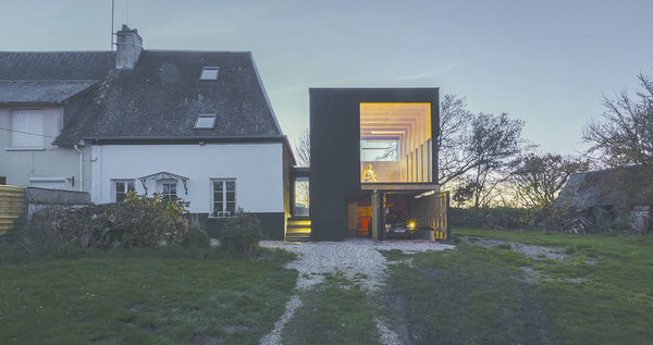 Cette extension de maison de campagne en bois de contreplaqué protégé par un goudron de pin noir, abrite, au rez-de-chaussée, un garage. Ouverte sur trois côtés, comme un observatoire, elle offre des vues sur le paysage changeant de la Normandie. Réalisation Antonin Ziegler.