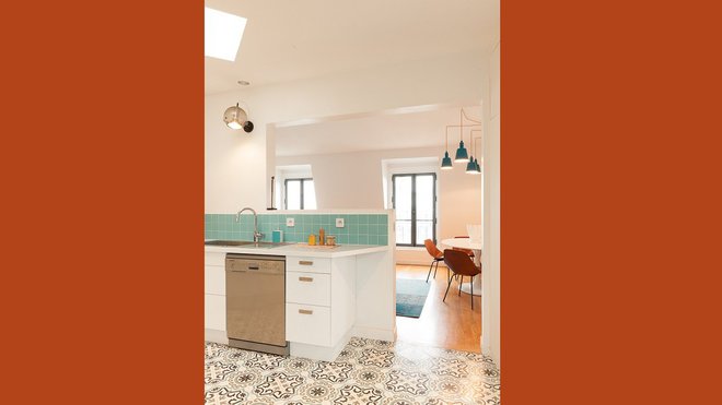 Le sol en carreaux de ciment délimite le périmètre de la cuisine cloisonnée par les éléments de rangement et la crédence en carrelage. Un luminaire vintage a été monté en applique.