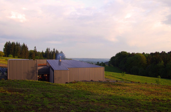 Surplombé par un chemin de grande randonnée, le bâtiment se tapit dans un creux du terrain pour conserver une vue dégagée. Construite dans un grand champ, ses couleurs aux tons d’ardoise font écho aux habitations environnantes.
