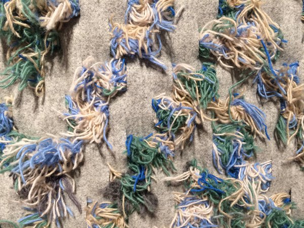 Nomad évoque une peau de mouton, contraste entre les fils de laine cousus dans le tissu. Le design de ce tapis s'est formé progressivement par la création de motifs conjuguant tissage, motifs croisés et chevrons.