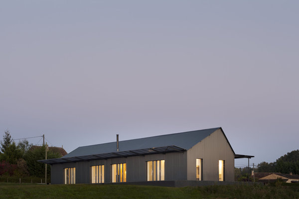 L’enveloppe de la façade est revêtue d’un bardage métallique ondulé gris foncé, évoquant la couleur des séchoirs à tabac locaux.