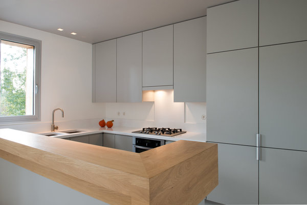 La cuisine s’intègre parfaitement dans l’espace avec un bar en bois clair qui délimite la zone de préparation des repas. Ouverte sur la salle à manger, elle conserve son intimité grâce à un jeu de volumes, couleurs et matières. Les éléments techniques et les nombreux rangements sont dissimulés pour respecter la pureté des lignes que l’éclairage accentue.