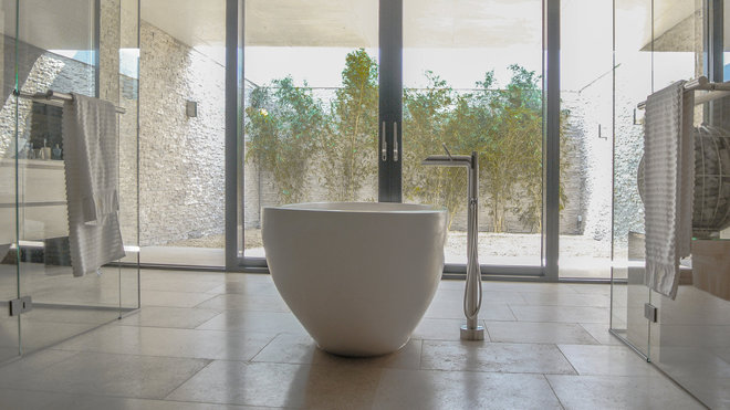Dans la salle de bains, habillée de pierre et de verre et donnant sur un  patio, on a joué avec l’effet de transparence et la communication avec l’extérieur pour offrir encore plus de profondeur à l’espace.