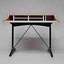 Ce bureau de dame CM 193 a été édité par Thonet en 1959. Sa forme originale reprend les codes d’un secrétaire ancien avec range-courrier, mais sans cylindre ni abattant. Il est posé sur un piétement en I, profilé et laqué noir, extrêmement moderne. Le code couleur : noir, blanc, gris et merisier lui confère un aspect très chic et raffiné pour un usage domestique. On peut le comparer au modèle de Georges Nelson. En métal laqué, bois laqué, laiton, merisier et moleskine.