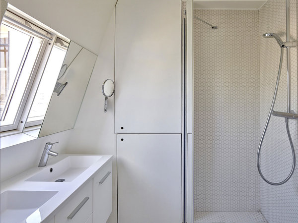 La salle de bains blanche joue la carte de la discrétion avec des rangements qui épousent les murs.