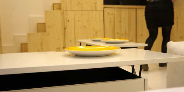 Au centre de l’espace, un podium-coffre s’ouvre pour offrir un espace de rangement. Les portes qui se soulèvent servent de table. On a suffisamment d’espace  pour intégrer des sièges.