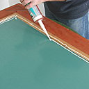 ​Etape 8 : dépose d’un cordon de colle silicone sur le bord du miroir au pourtour, ainsi qu’un cordon sur la partie en bois du cadre.