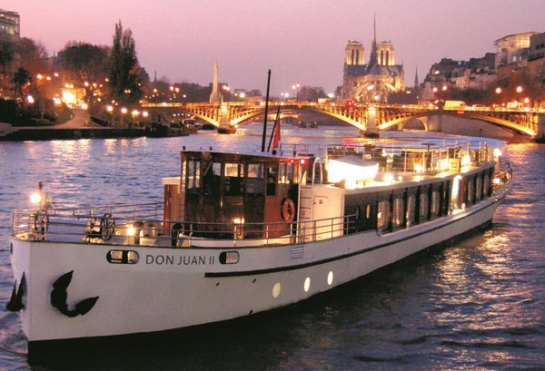 À la tombée de la nuit, le Dom Juan II fait partie du paysage féérique et pittoresque de la Seine avec vue sur la cathédrale Notre-Dame.