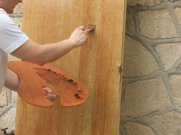 Etape 13 : Sur la palette, placer les couleurs à l’huile en tubes suivantes : terre d’Ombre brûlée, terre d’Ombre naturelle, terre de Sienne naturelle, bleu outremer, laque carminée. Puis, avec un spalter à dents, mettre en teinte la porte avec les couleurs en mélange de deux à trois teintes. Le geste sera plus ou moins linéaire sur le long de la porte.