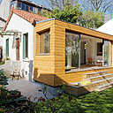 La structure bois de l’extension sud s’intègre parfaitement à l’ancienne. La longue terrasse étroite fait le lien entre l’extension sud et le jardin, sans réduire les espaces verts. Elle offre une transition judicieuse avec le salon plus haut de 5 marches et se transforme à l’occasion en banquette avec des coussins de sol colorés.