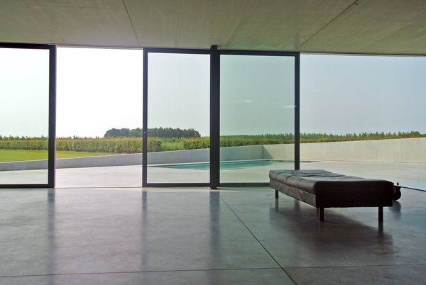 Le salon s’ouvre sur la terrasse et la piscine intégrées dans le volume de la maison, mais dissimulées derrière un mur en pente.