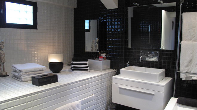 La salle de bains joue la carte de l’Art déco. Le choix du noir et blanc, avec un effet bicolore graphique très marqué, symbole de modernité dans les années 1930, se retrouve jusque dans les accessoires de toilette. Un large plan carrelé blanc fait écho à la baignoire située de l’autre côté.