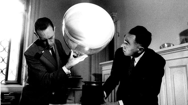 Créée en 1958, la lampe nécessita quelques années de mise au point par les frères Achille et Pier Giacomo Castiglioni, immortalisés ici en 1962.