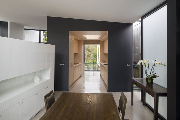 La cuisine insérée dans une coquille intérieure, avec ses deux murs de rangement parallèles, comme un couloir, dessine un espace traversant en continuité de l’espace salle à manger, délimité par le mobilier. Cette pièce à vivre fait le lien entre l’avant,côté rue, et l’arrière de la maison côté jardin.
