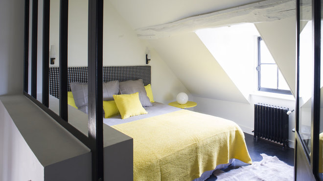 Une pointe de jaune soleil illumine la chambre sous les toits, avec une verrière d’atelier, comme cloison de séparation.