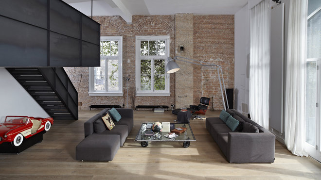 Le salon en enfilade est matérialisé par deux canapés qui se font face. L’espace au sol est libéré pour faciliter la communication. Fauteuil Lounge Chair, création Ray et Charles Eames, en 1954, éditée chez Vitra. Lampadaire, Anglepoise. Placés sous les fenêtres, des radiateurs industriels s’intègrent au décor.