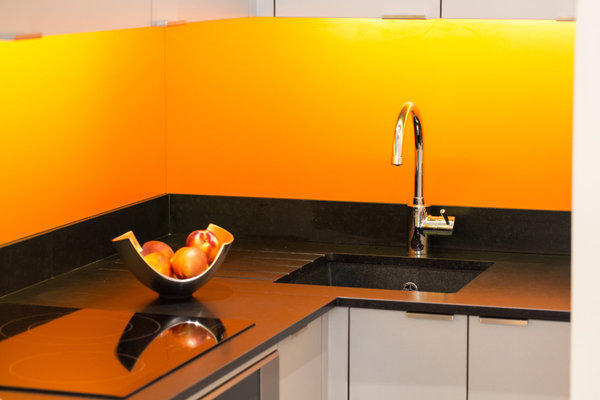 Dans la cuisine, le plan de travail sombre en angle fabriqué en granit du Zimbabwe contraste avec la crédence en stratifié orange.