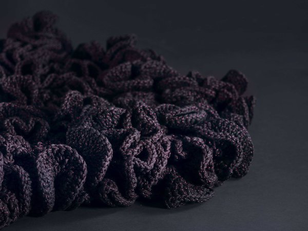 Gros plan sur la tapis fleur avec fil violet ponctué de rouge contenant différentes matières et fibres.
