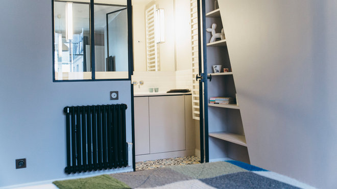 Une niche avec étagères a été pratiquée en continuité du coffrage de la cheminée. Les radiateurs peints en noir s’accordent avec les châssis de la verrière de la salle de bains. Sol de la salle de bains en carreaux ciment, Mosaic del Sur.