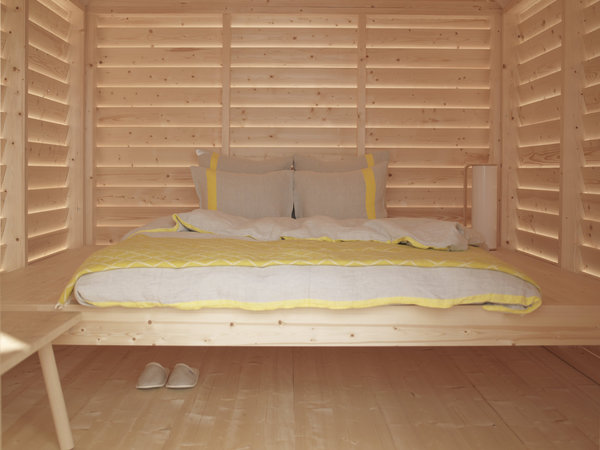 Le lit surélevé est une plateforme en bois, entourée de persiennes, qui laissent filtrer la lumière naturelle.