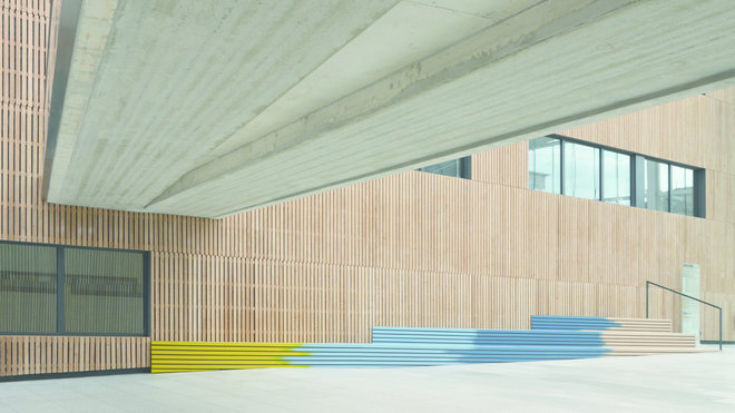 Dans l’entrée, des bancs en gradins à double fonction ont été implantés. Ils épousent le sol en pente et apportent une dynamique colorée à l’espace. Dans l’entrée, des bancs en gradins à double fonction ont été implantés. Ils épousent le sol en pente et apportent une dynamique colorée à l’espace.