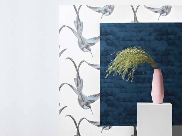 Envolée de colibris pour le papier peint Lintu coloris Ether disponible dans 4 autres couleurs (Emeraude, Patchouli, Safran et Magnolia) et motif Zhe, coloris Marine, disponible dans 3 autres couleurs (Jade, champagne et Jasmin).