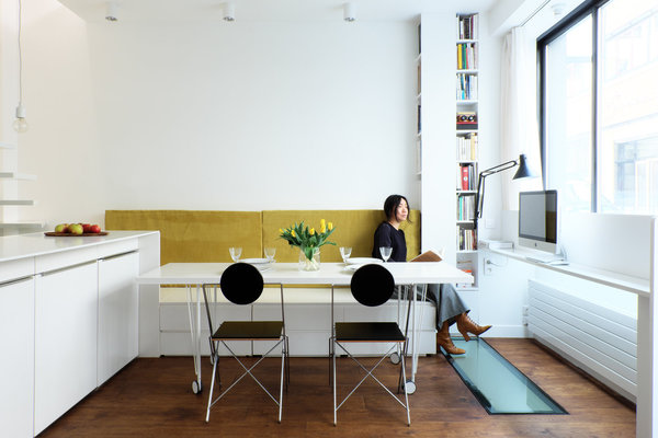 Unité inférieure à deux niveaux. Dans l’unité inférieure, une table à roulettes peut servir de table pour les repas. Le soir, quand le placard de la cuisine est ouvert et la table déplacée devant la banquette, le bureau se transforme en une salle à manger pour 6 à 8 personnes. A droite, troisième poste de travail et, au sol, une vitre pour éclairer le souplex.