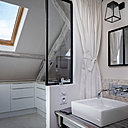 La salle de bains et la cuisine ont été aménagées dans l’entrée, en continuité du couloir qui mène à la pièce principale. La cuisine ouverte fait face à une porte coulissante en métal et verre de type industriel, qui permet de gagner de la place et de la lumière.