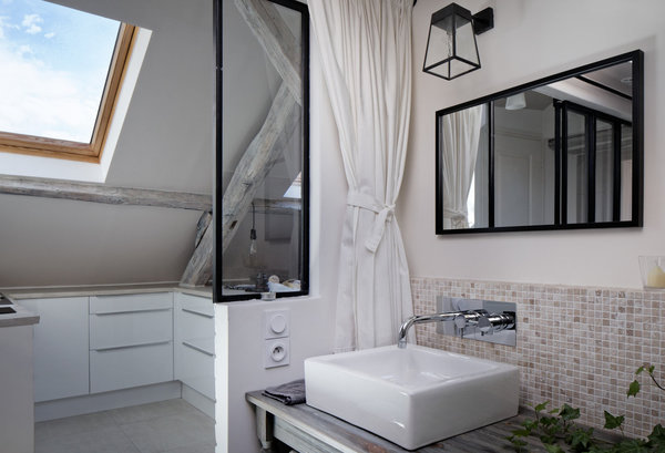 La salle de bains et la cuisine ont été aménagées dans l’entrée, en continuité du couloir qui mène à la pièce principale. La cuisine ouverte fait face à une porte coulissante en métal et verre de type industriel, qui permet de gagner de la place et de la lumière.