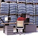 Bureau Quasinormal, interprétation contemporaine du bureau de direction avec des proportions et des matériaux d’aujourd’hui. Plateau en multiplis de coffrage bakélisé, caissons en acier plié avec tiroirs et étagères en laque martelée grise. La pièce de jonction des éléments permet des variations de positionnement. Blocs étagères et support pour écran avec finition « canon de fusil ». Lampe possible pour compléter l’ensemble. Création Jean Nouvel pour Bulo, en 1996.