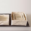 Sur un plateau, 3 boîtes pliées Origami façon gigogne en porcelaine papier émaillée (la plus grande : 10 x 9 cm). Création Caroline Worner.