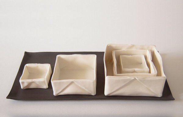 Sur un plateau, 3 boîtes pliées Origami façon gigogne en porcelaine papier émaillée (la plus grande : 10 x 9 cm). Création Caroline Worner.