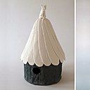 A gauche, nichoir avec base en terre noire colorée à l’oxyde de fer et empreinte d’écorce. Toit en porcelaine papier. A droite, vase cylindrique en biscuit brut mat avec intérieur émaillé, reprenant l’idée du tronc d’arbre. Créations Caroline Worner.