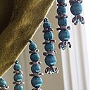 Revisitée. Une collection tout en élégance, qui réinterprète la géométrie et la pureté des lignes du style Art déco avec deux nouveaux coloris, turquoise et nude. Frange perles et embrasse un gland, 12 coloris, collection Palladio, Houlès.