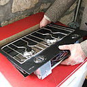 Etape 6 : Positionner la table dans le trou afin de vérifier qu’elle s’encastre correctement et sans forcer. Au besoin ajuster la découpe à l’aide de la scie. Retourner la table et raccorder une des extrémités du flexible de gaz à la plaque de cuisson en serrant bien les écrous à l’aide d’une clé et d’une contre clé.