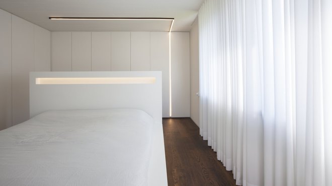 Des murs de rangement habillent les chambres immaculées et dotées d’un système d’éclairage linéaire. Le mobilier laqué blanc joue les effets de contraste avec le chêne teinté wengé du parquet (Parquet Gallery, www.parquetgallery.be). Rideaux chez Mooi Wonen (www.mooiwonnen.be)